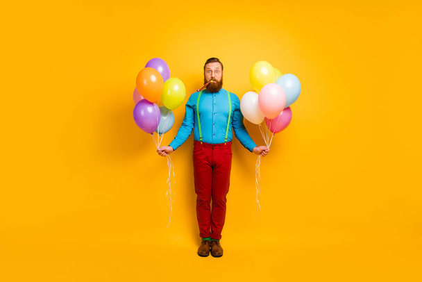 Full size photo of funny funky imposing hold many helium baloons whistle party noisemaker celebrate enjoy anniversary wear green blue clothes footwear isolated over yellow color background - 写真・画像