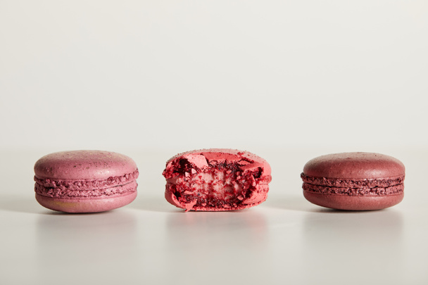 delicious whole and one bitten red french macaroons on white background - Photo, Image