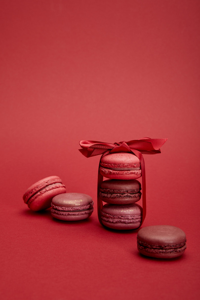 delicious colorful french macaroons wrapped in ribbon with bow on red background - Valokuva, kuva