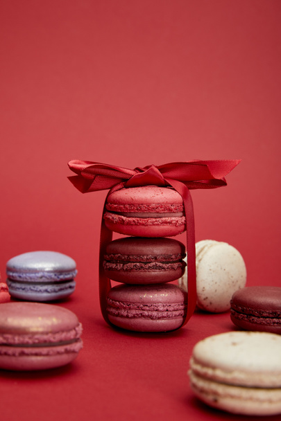 assorted delicious colorful french macaroons with bow on red background - Foto, afbeelding