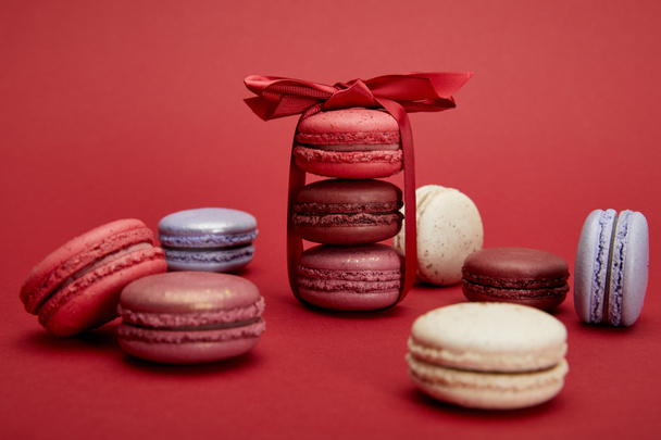 assorted delicious colorful french macaroons with bow on red background - Photo, Image