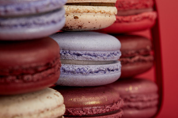 stack of assorted delicious colorful french macaroons on red background - Foto, afbeelding