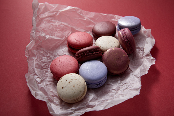 assorted delicious colorful french macaroons on crumpled paper on red background - Foto, afbeelding