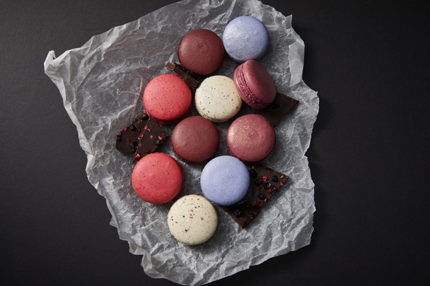 top view of assorted delicious colorful french macaroons on crumpled paper with chocolate on black background - Photo, Image