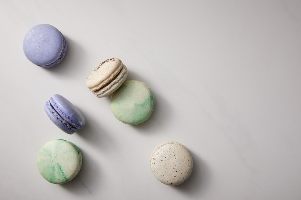 top view of assorted delicious green, violet and white  french macaroons on grey background - Фото, изображение