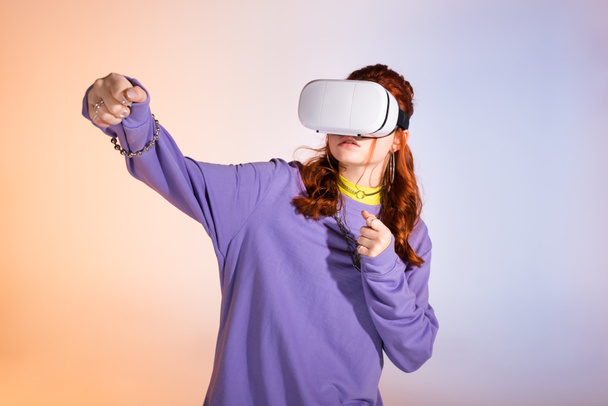 emotional teen girl gesturing and using virtual reality headset, on purple and beige  - Zdjęcie, obraz