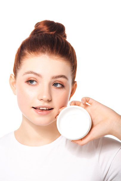 pozytywna nastolatka z idealną skórą trzymającą plastikowy pojemnik z kremem kosmetycznym, izolowana na biało - Zdjęcie, obraz