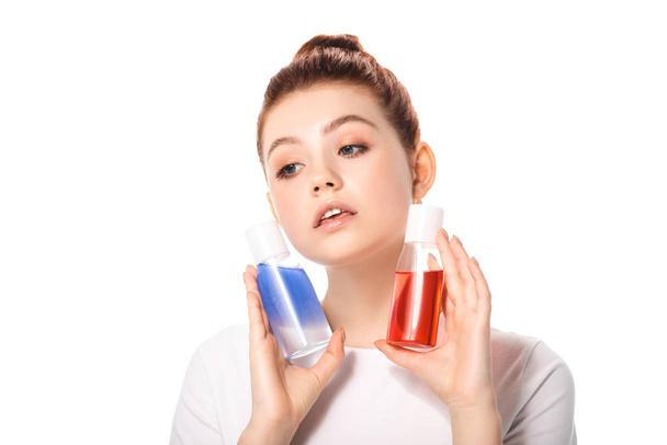 beautiful teenager holding two bottles with red and blue makeup removers, isolated on white - Zdjęcie, obraz
