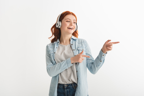 excited teen girl listening music with headphones and pointing isolated on white - Fotografie, Obrázek