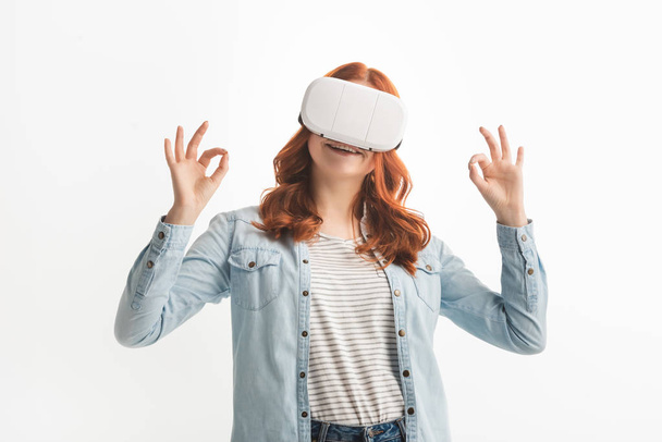 улыбчивый рыжеволосый подросток, показывающий хорошие признаки и использующий гарнитуру VR, изолированную на белом
 - Фото, изображение