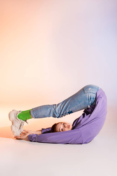 sad redhead female teenager lying with legs up, on purple and beige   - Zdjęcie, obraz