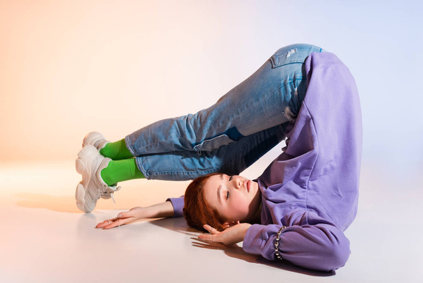 bored redhead female teenager lying with legs up, on purple and beige  - Фото, изображение
