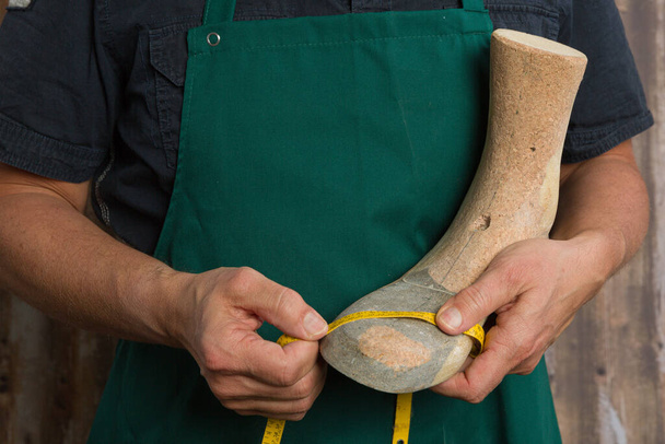 Nahaufnahme orthopädischer Schuhmacherhände mit Maßband und Holzleiste  - Foto, Bild