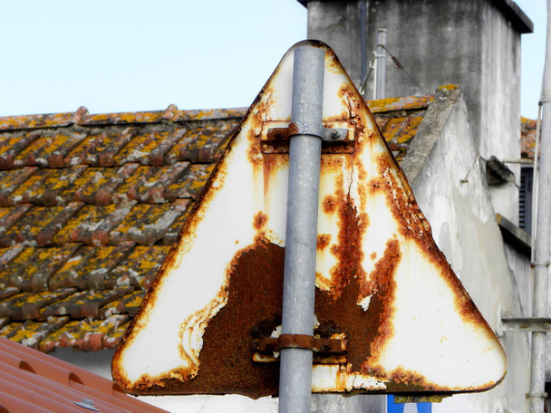 very rusty triangle shaped traffic sign due to salty air. The back of a rusty street sign on a pole - Photo, Image