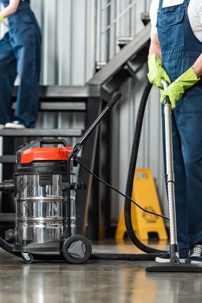 cropped view of cleaner vacuuming floor near colleague cleaning stairs - 写真・画像