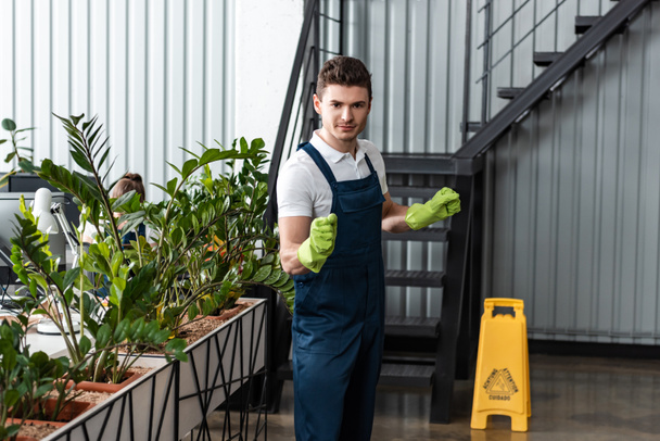 handsome young cleaner in overalls and rubber gloves looking at camera - Photo, Image