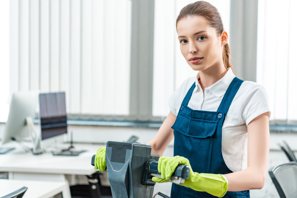attractive cleaner in overalls looking at camera while standing with cleaning machine - Photo, Image
