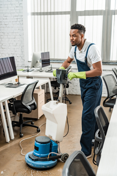 Yakışıklı Afro-Amerikan temizleyici ofiste temizlik makinesiyle yerleri yıkıyor. - Fotoğraf, Görsel