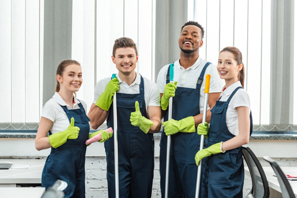 happy multicultural team of cleaners looking at camera and showing thumbs up - Photo, Image