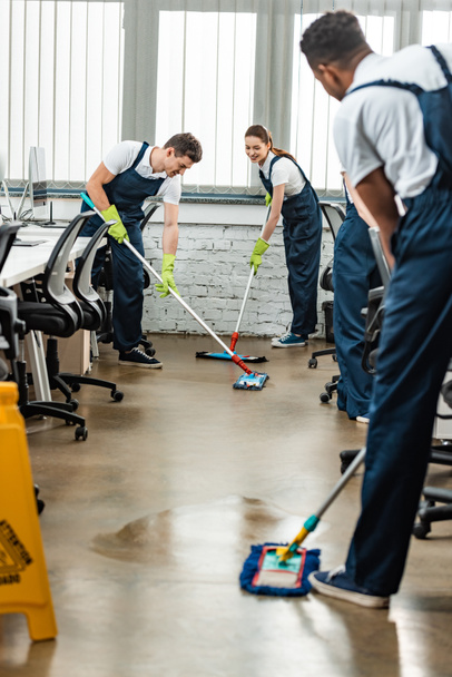 multicultural team of young cleaners washing floor with mops in office - Photo, Image