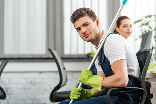 handsome cleaner sitting in office chair near attractive colleague - Foto, imagen