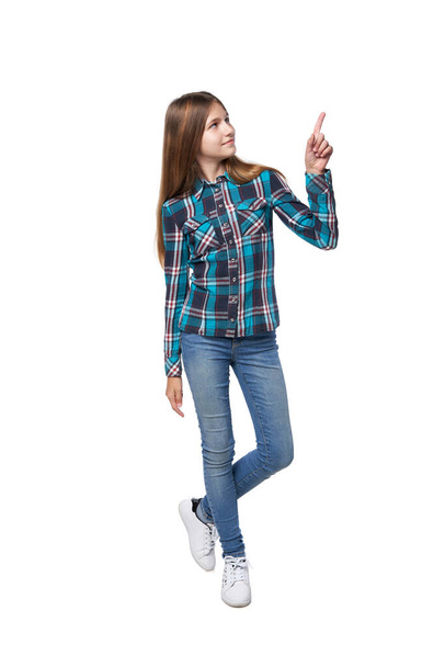 Full length teen girl in checkered shirt standing casually over white background pointing up - Zdjęcie, obraz