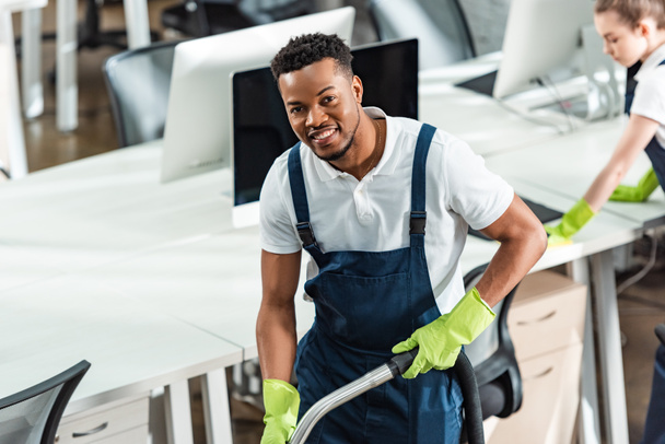 smiling african american cleaner looking at camera near young colleague - Photo, Image