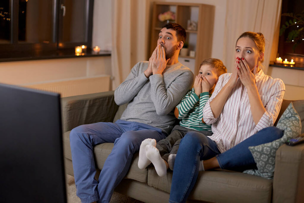 испуганная семья смотрит телевизор дома по ночам
 - Фото, изображение