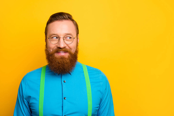 Closeup photo of funny red head guy beaming smiling elegant clothes look side empty space wear specs bright blue shirt green suspenders isolated yellow color background - Foto, Imagem