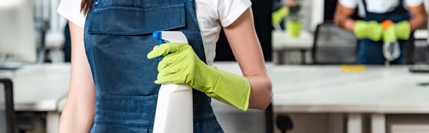 обрезанный вид молодой уборщицы в комбинезоне, держащей баллончик с моющим средством
 - Фото, изображение