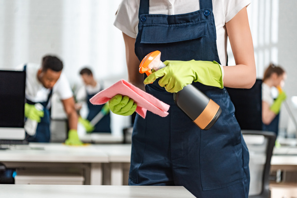 cropped view of cleaner in uniform spraying detergent on rag - 写真・画像