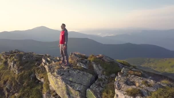 Turysta stojący na szczycie skalistej góry cieszący się wspaniałym widokiem. Alpinista patrzy na wschód słońca w górach. - Materiał filmowy, wideo
