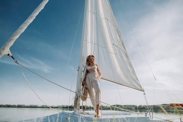 Woman stands on a yacht with white sails and looks at the sunset. Model on vacation on a yacht - Photo, Image
