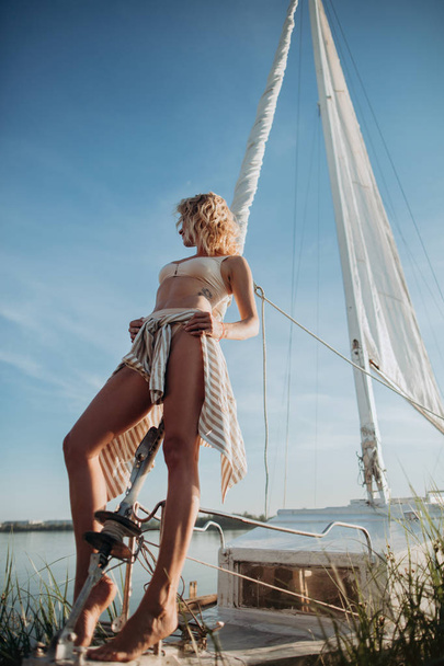 Žena stojí na jachtě s bílými plachtami a dívá se na západ slunce. Model na dovolené na jachtě - Fotografie, Obrázek