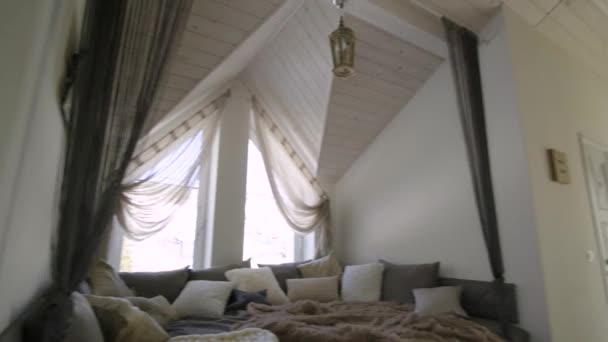 Modern bir evin içi geniş bir koridor ve büyük yumuşak bir dinlenme yeri. Çağdaş geniş kanepe, çok yastıklı ve pencereli ahşap tavan.. - Video, Çekim