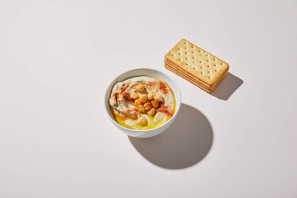 Bowl with delicious hummus near crackers on grey background - Photo, Image