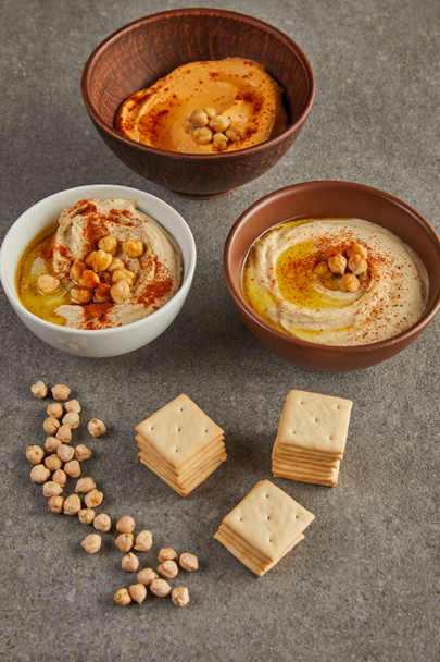 Bowls with tasty hummus with chickpea and crackers on grey background - Photo, Image