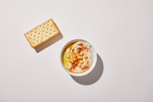 Bovenaanzicht van kom met lekkere hummus en crackers op grijze achtergrond - Foto, afbeelding