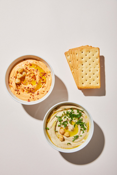 Top view of bowls with delicious hummus and crackers on grey background - Foto, Bild