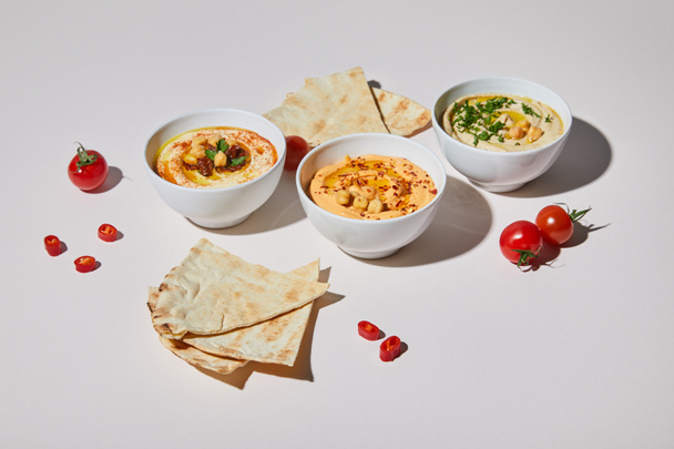 Bowls with hummus, ripe vegetables and pita bread on grey background - Foto, immagini