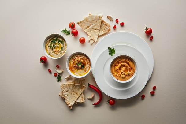 Schleppblick auf Teller, Schüsseln mit leckerem Hummus, frischem Gemüse und Fladenbrot auf grauem Hintergrund - Foto, Bild