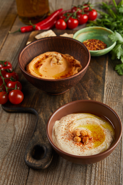 Selective focus of bowls with paprika and hummus, vegetables and parsley on wooden background - Fotoğraf, Görsel