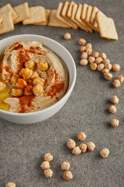Selective focus of bowl with tasty hummus, chickpea and crackers on grey background - Fotografie, Obrázek