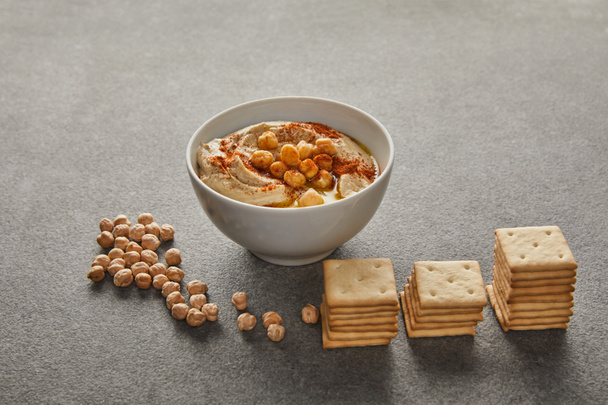 Bowl with delicious hummus, chickpea and crackers on grey  - Photo, Image