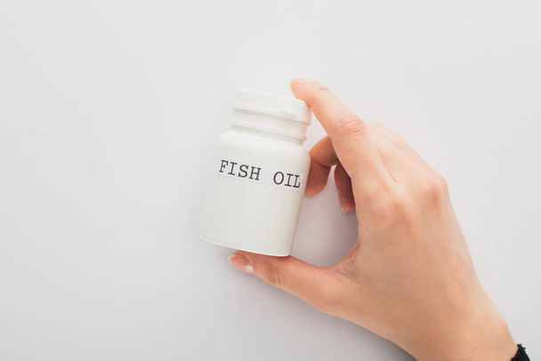 Cropped view of woman holding container with fish oil lettering on white background - Photo, Image