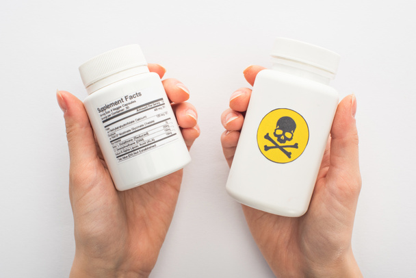 Vista cortada da mulher segurando recipientes com suplementos dietéticos e veneno perigoso no branco
  - Foto, Imagem