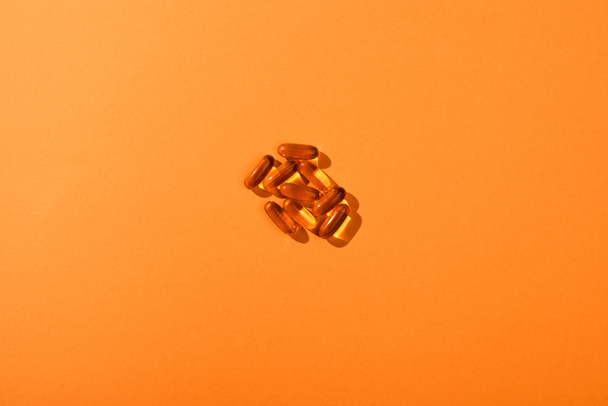 Bovenaanzicht van bruine capsules op oranje achtergrond - Foto, afbeelding