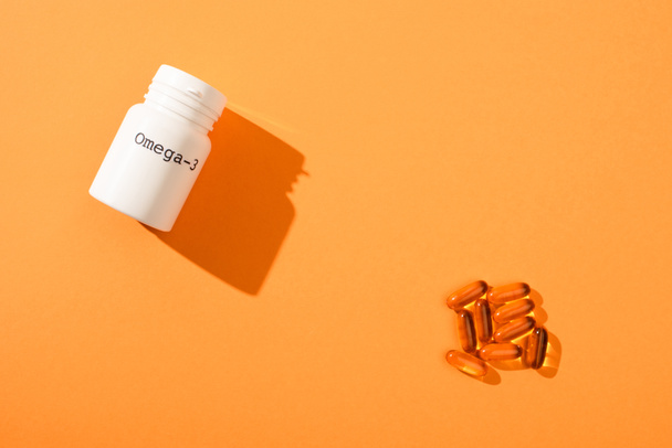 Bovenaanzicht van container met omega-3 belettering en capsules op oranje achtergrond - Foto, afbeelding