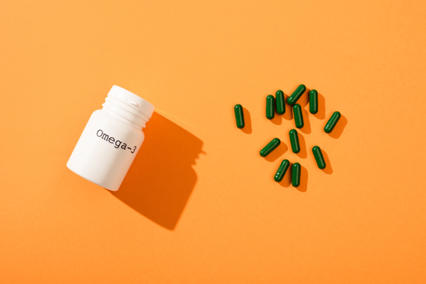 Top view of container with omega-3 lettering and green capsules on orange background - Foto, afbeelding