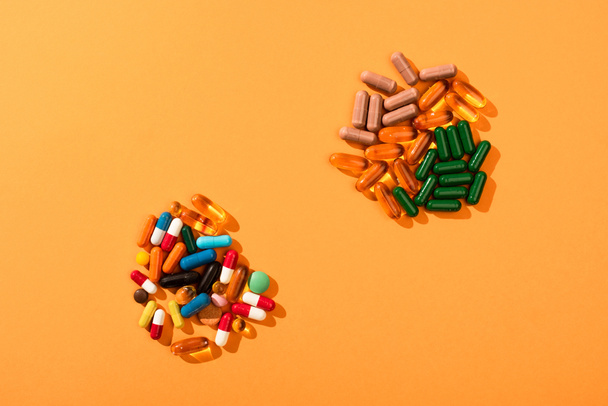 Верхний вид красочных таблеток и капсул на оранжевом фоне
 - Фото, изображение